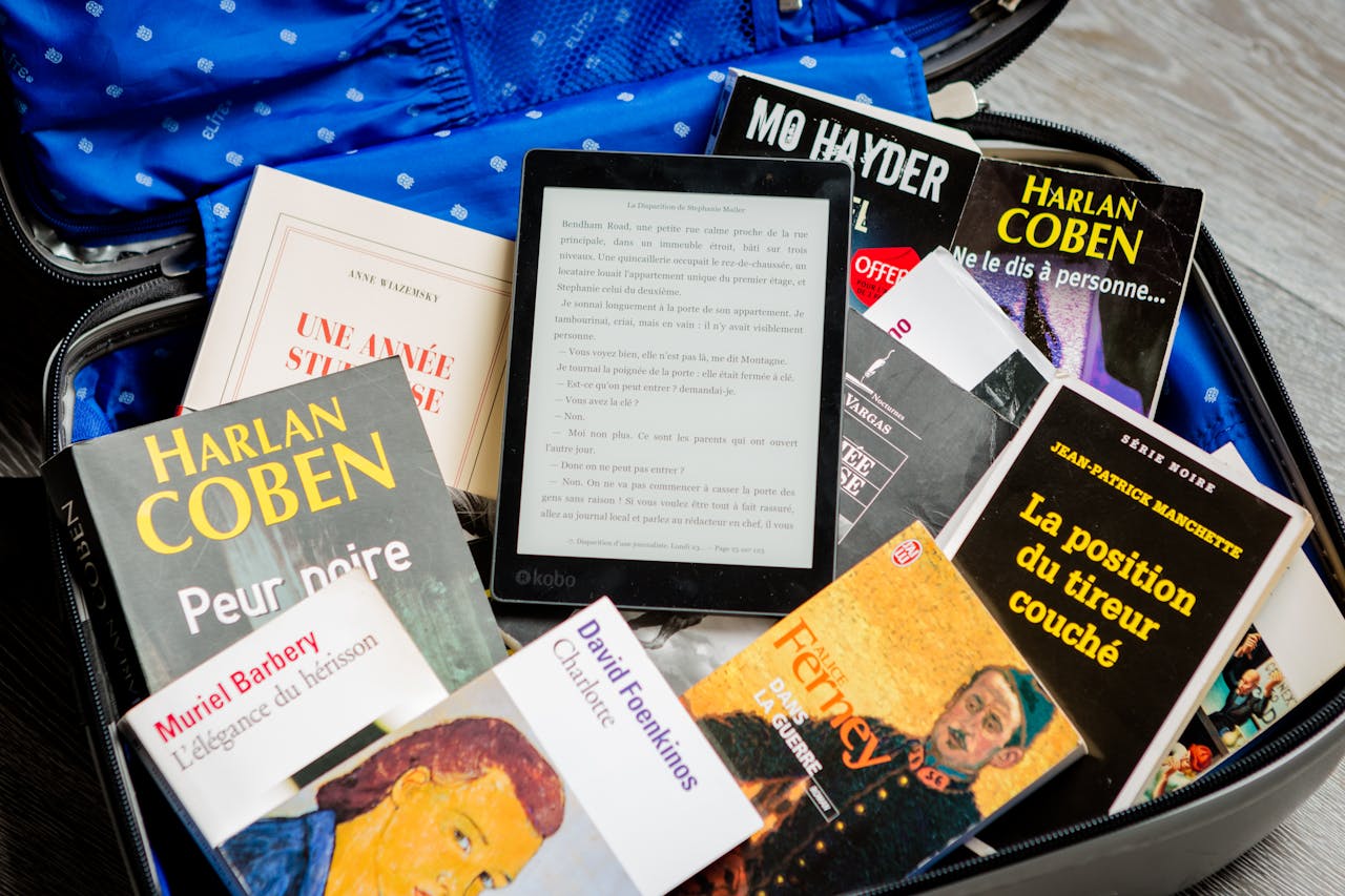 A mix of paperback books and an e-reader neatly packed in an open suitcase for travel.